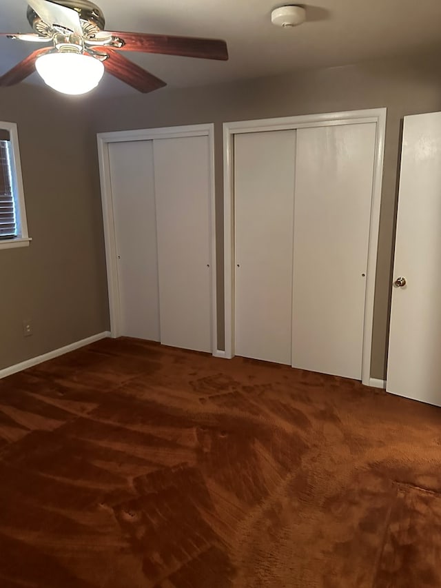 unfurnished bedroom featuring dark colored carpet, two closets, and ceiling fan