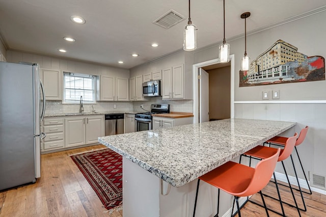 2607 N N St, Midland, TX 79705 - kitchen with a kitchen breakfast bar, visible vents, crown molding, a sink, and stainless steel appliances