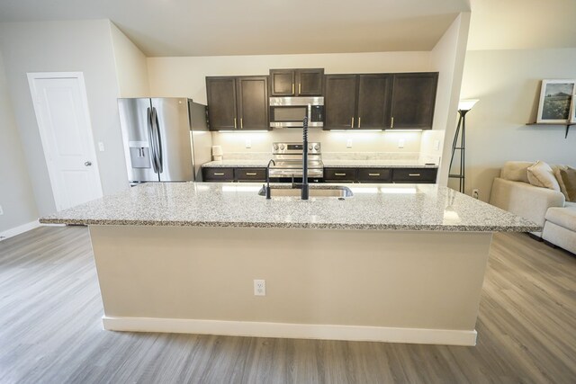 2908 Stagecoach Ct, Midland, TX 79705 - kitchen featuring stainless steel appliances, dark brown cabinetry, wood finished floors, and an island with sink