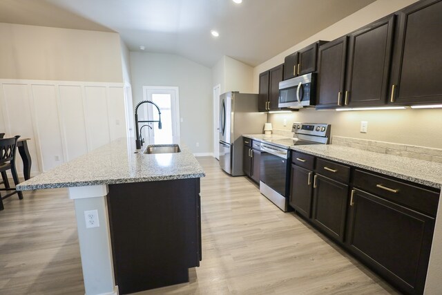 2908 Stagecoach Ct, Midland, TX 79705 - kitchen with appliances with stainless steel finishes, an island with sink, light wood-style floors, vaulted ceiling, and light stone countertops