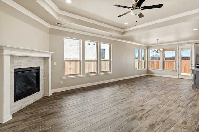 unfurnished living room featuring ceiling fan with notable chandelier, a tiled fireplace, hardwood / wood-style flooring, and a tray ceiling