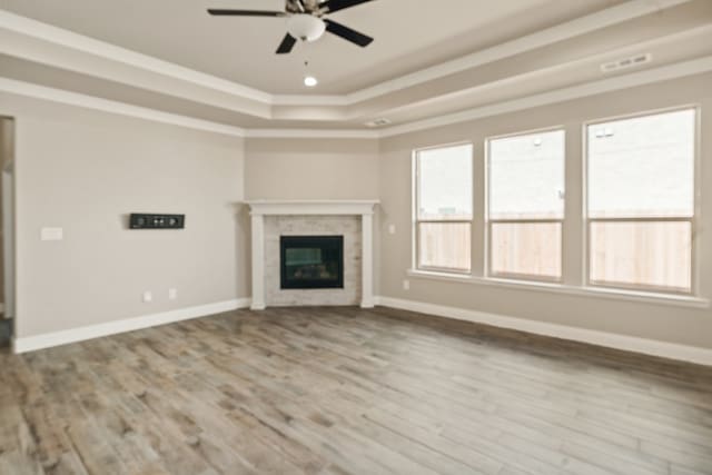 unfurnished living room with ceiling fan, a tray ceiling, and light hardwood / wood-style flooring