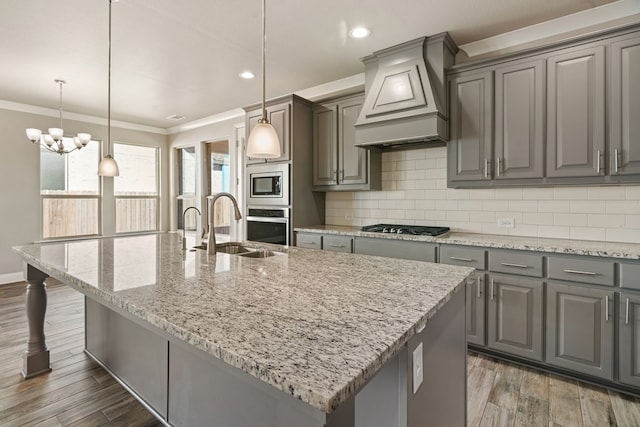 kitchen featuring a center island with sink, custom exhaust hood, hanging light fixtures, and light stone countertops