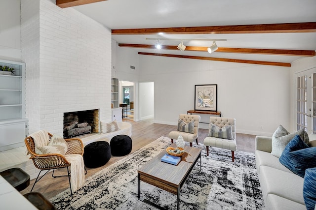 living room featuring light wood-type flooring, vaulted ceiling with beams, track lighting, and a brick fireplace