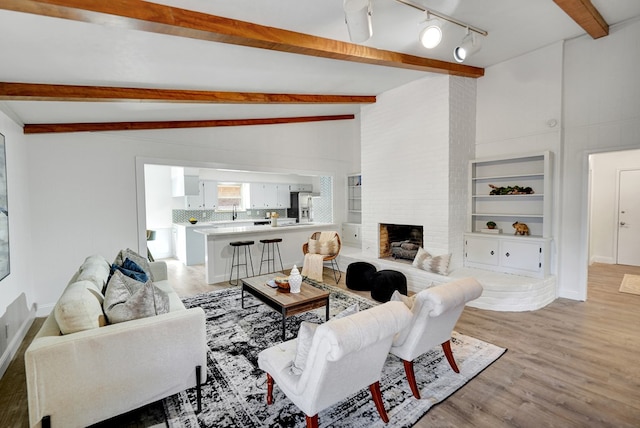 living room featuring a fireplace, light wood-type flooring, and vaulted ceiling with beams