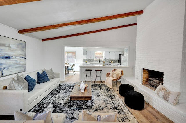 living room with hardwood / wood-style floors, lofted ceiling with beams, and a brick fireplace