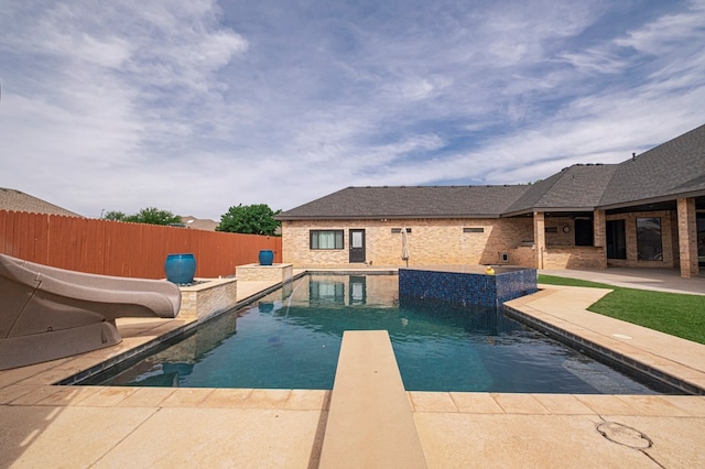 view of swimming pool with a water slide, fence, a patio area, and a diving board