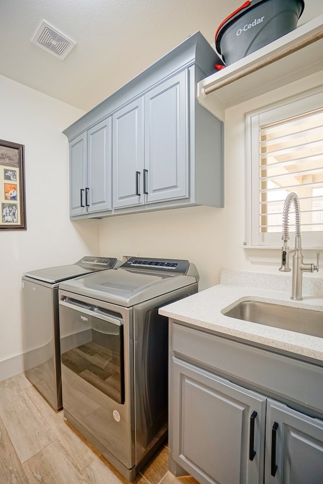 clothes washing area with cabinets, light wood-type flooring, sink, and washing machine and clothes dryer