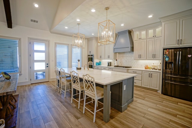 kitchen featuring pendant lighting, a kitchen island with sink, light hardwood / wood-style flooring, custom range hood, and stainless steel appliances