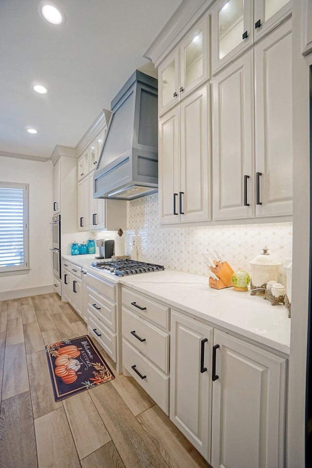 kitchen with light hardwood / wood-style flooring, white cabinets, stainless steel appliances, and custom range hood