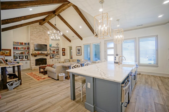 kitchen featuring a fireplace, decorative light fixtures, light hardwood / wood-style floors, and an island with sink