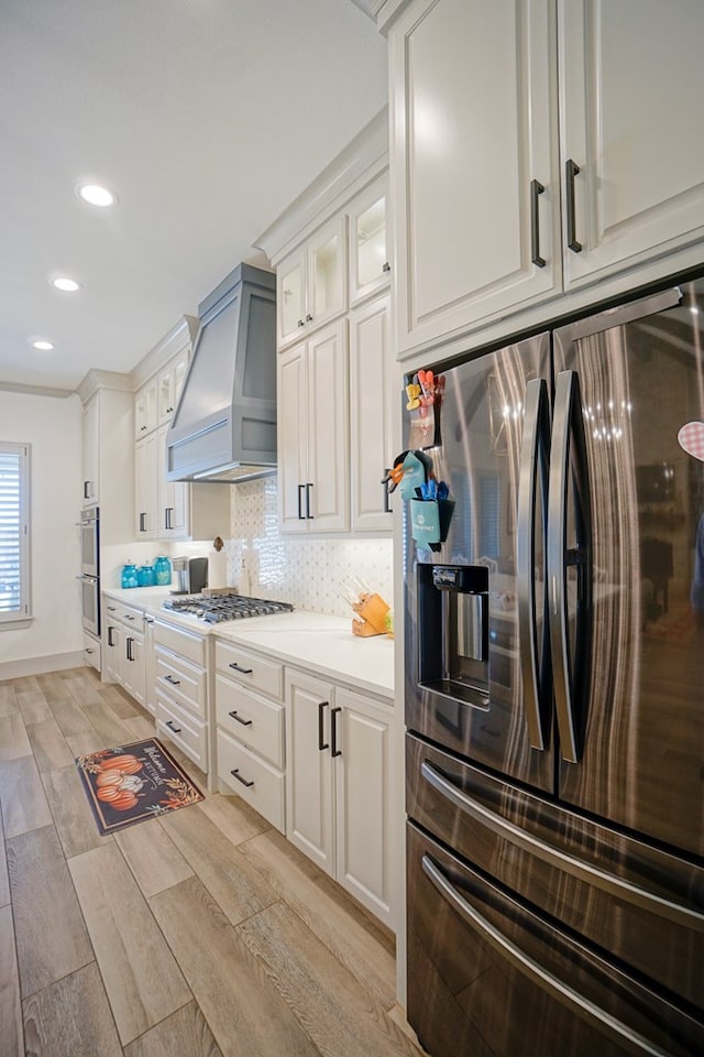 kitchen featuring custom range hood, light wood-type flooring, stainless steel appliances, and white cabinetry