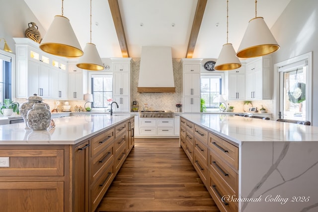 kitchen with hanging light fixtures, white cabinetry, custom range hood, and a large island with sink