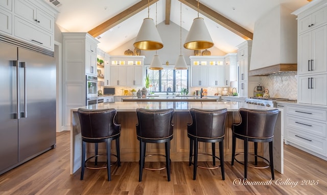 kitchen featuring stainless steel appliances, premium range hood, pendant lighting, and white cabinetry