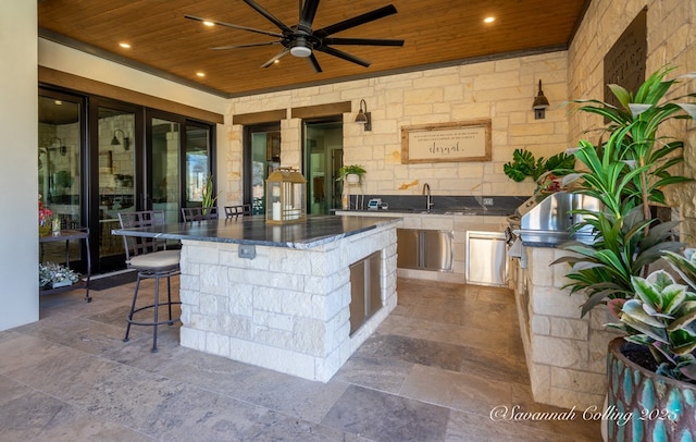 view of patio / terrace featuring a bar, ceiling fan, and an outdoor kitchen