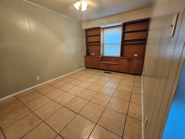 tiled spare room with a textured ceiling, ceiling fan, and wood walls