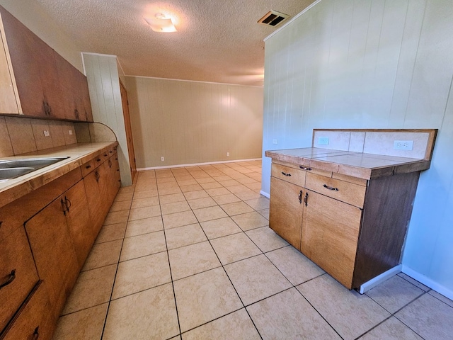 kitchen featuring wooden walls, sink, light tile patterned floors, and a textured ceiling