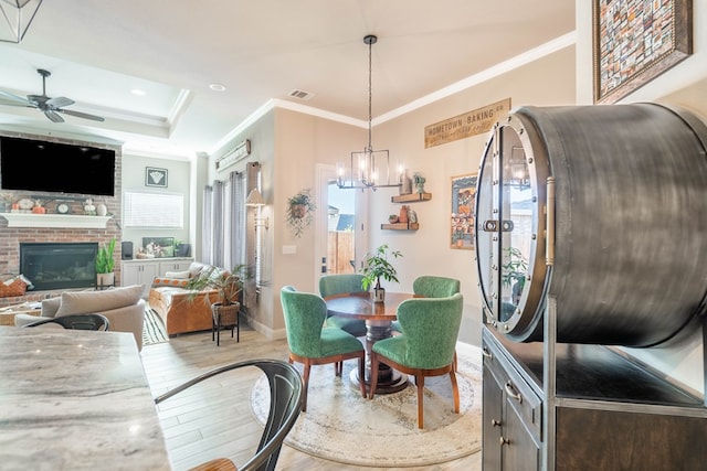 dining space featuring a brick fireplace, plenty of natural light, ornamental molding, and light wood-type flooring