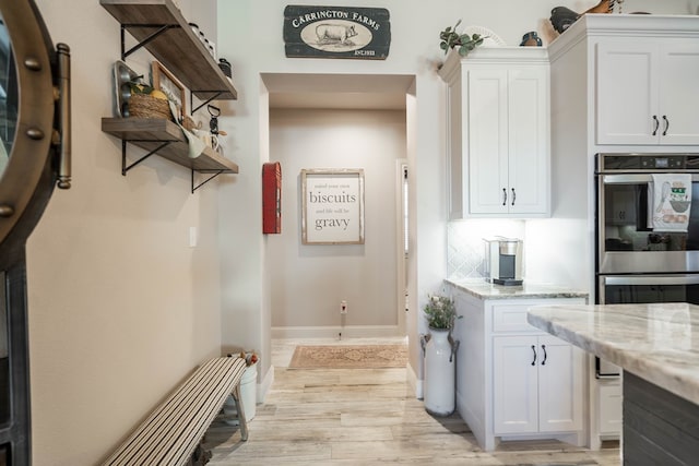 kitchen with white cabinets, light hardwood / wood-style flooring, decorative backsplash, light stone countertops, and stainless steel double oven