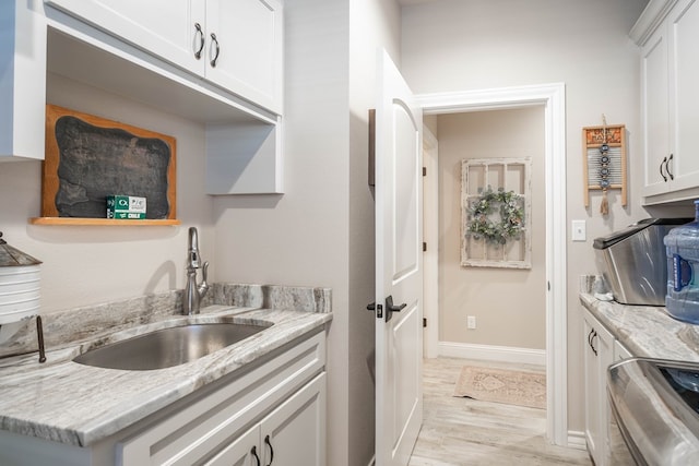 kitchen with white cabinetry, sink, light stone counters, light hardwood / wood-style flooring, and stainless steel stove