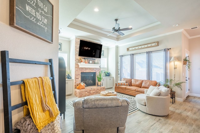 living room featuring ceiling fan, light hardwood / wood-style floors, a tray ceiling, a fireplace, and ornamental molding