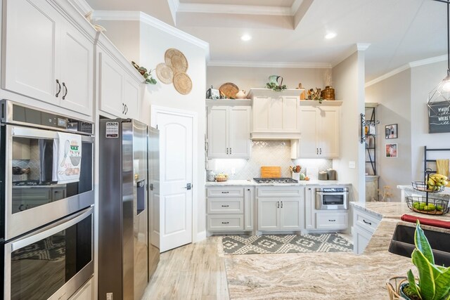 kitchen featuring light wood-type flooring, stainless steel appliances, crown molding, white cabinets, and hanging light fixtures