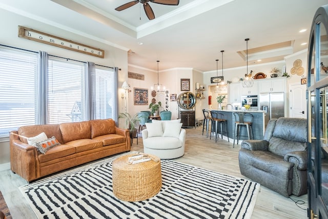 living room featuring ceiling fan with notable chandelier, light wood-type flooring, and a raised ceiling