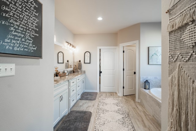 bathroom with wood-type flooring, vanity, and tiled bath