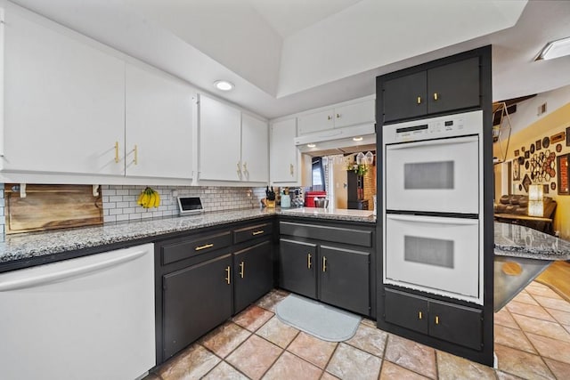 kitchen featuring white appliances, decorative backsplash, light stone countertops, a tray ceiling, and white cabinetry