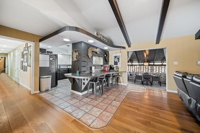 kitchen featuring a kitchen breakfast bar, stainless steel fridge, light hardwood / wood-style flooring, and beamed ceiling