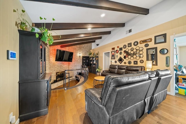 living room with vaulted ceiling with beams, hardwood / wood-style flooring, a brick fireplace, and brick wall