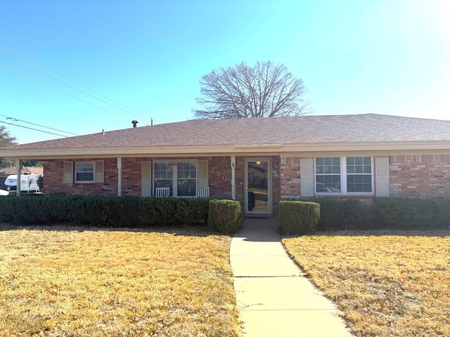 ranch-style home featuring brick siding, a front yard, and roof with shingles