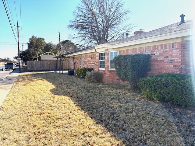 view of property exterior with a yard, fence, brick siding, and a chimney