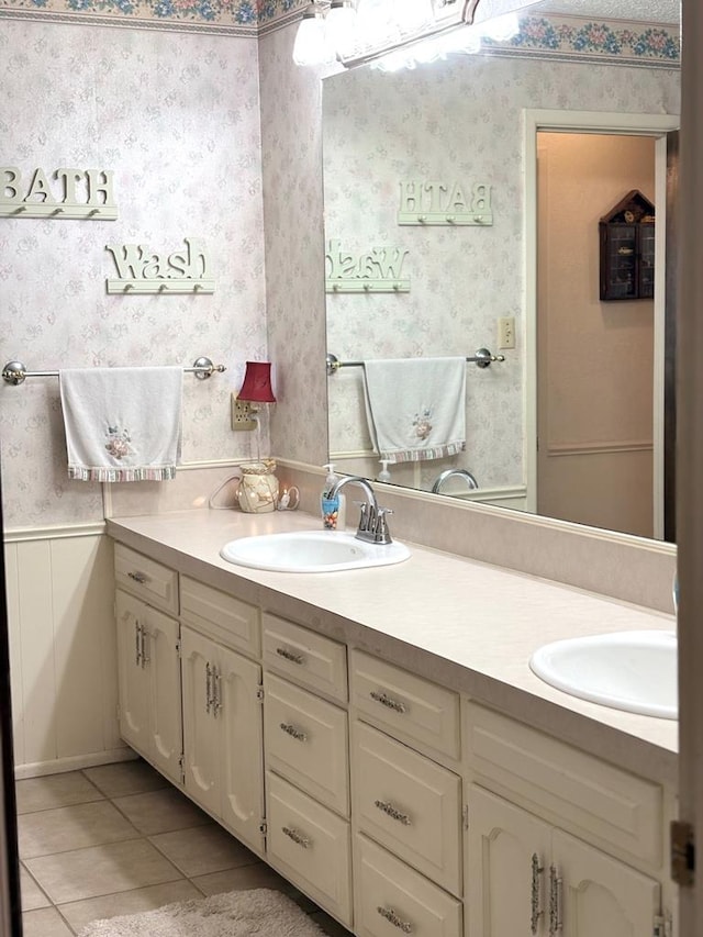 full bath with a sink, double vanity, wainscoting, and wallpapered walls