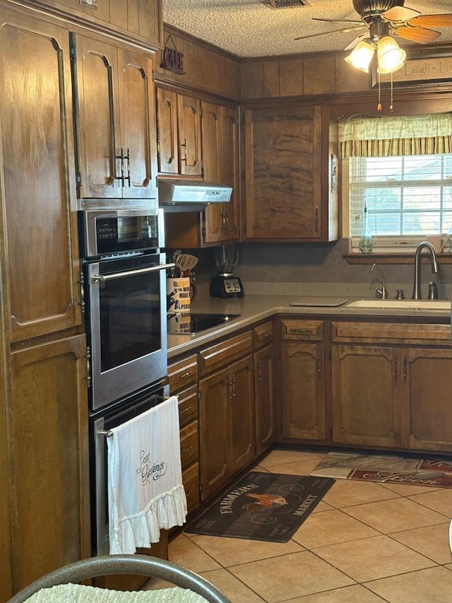 kitchen with black electric stovetop, under cabinet range hood, light tile patterned flooring, a ceiling fan, and a sink