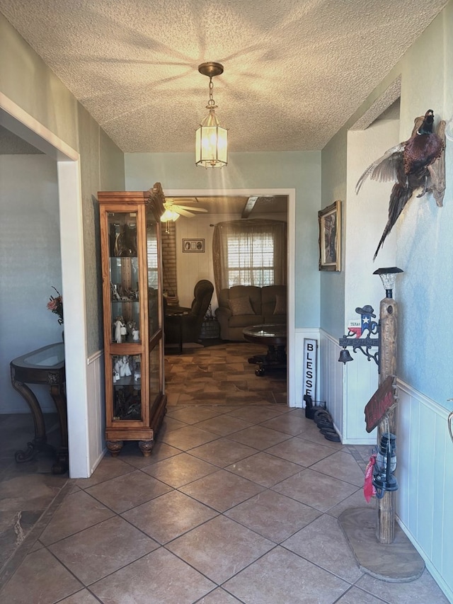 hallway with a textured ceiling, tile patterned floors, and wainscoting