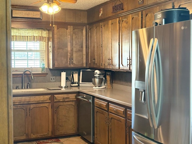 kitchen featuring a ceiling fan, a sink, brown cabinetry, stainless steel fridge with ice dispenser, and light countertops