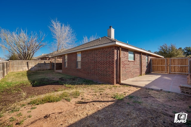 view of side of property featuring a fenced backyard, brick siding, a lawn, a chimney, and a patio area