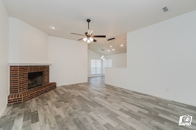 unfurnished living room featuring ceiling fan, lofted ceiling, wood finished floors, visible vents, and a brick fireplace