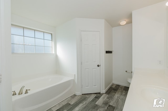 bathroom featuring toilet, a sink, wood finished floors, and a bath