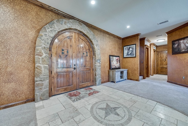 foyer entrance with arched walkways, ornamental molding, visible vents, and stone tile floors