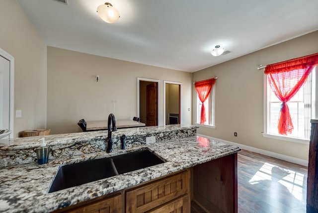 kitchen featuring light stone countertops, a sink, baseboards, and wood finished floors