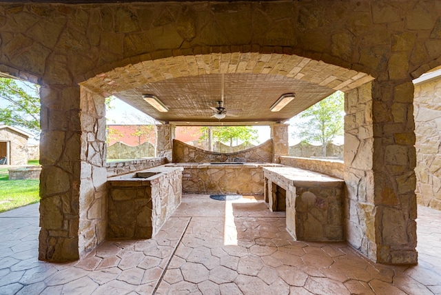 view of patio with ceiling fan, an outdoor stone fireplace, and area for grilling