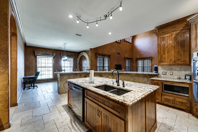 kitchen with dishwashing machine, stone tile flooring, a sink, stainless steel microwave, and a center island with sink