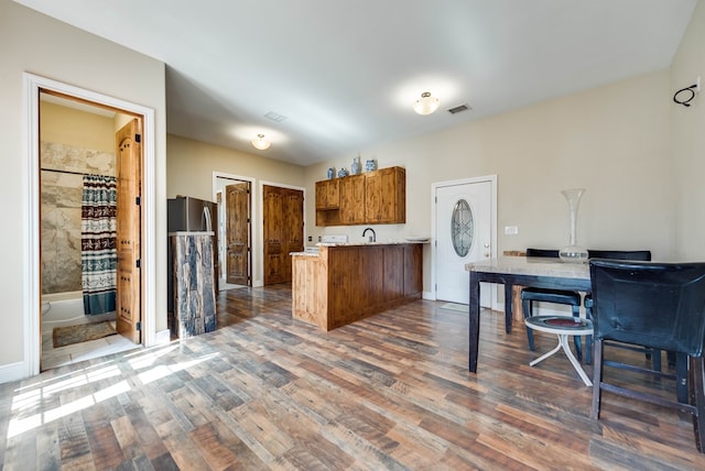 kitchen with dark wood-style flooring, brown cabinets, light countertops, visible vents, and a peninsula