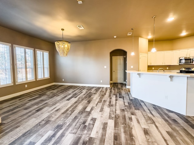 kitchen with pendant lighting, white cabinets, wood-type flooring, and stainless steel appliances