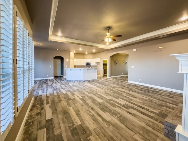 unfurnished living room with ceiling fan, wood-type flooring, crown molding, and a tray ceiling