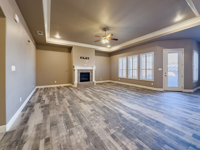 unfurnished living room featuring crown molding, ceiling fan, wood-type flooring, and a brick fireplace