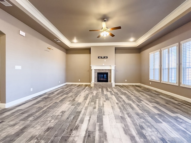 unfurnished living room with ceiling fan, a raised ceiling, crown molding, a fireplace, and hardwood / wood-style flooring