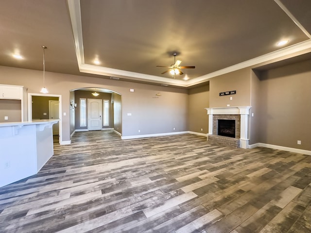 unfurnished living room with ceiling fan, a fireplace, ornamental molding, and dark wood-type flooring